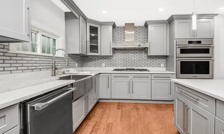 Kitchen with stainless steel appliances, backsplash, gray cabinetry, and wall chimney exhaust hood