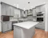 Kitchen with gray cabinets, stainless steel appliances, a kitchen island, wall chimney exhaust hood, and tasteful backsplash