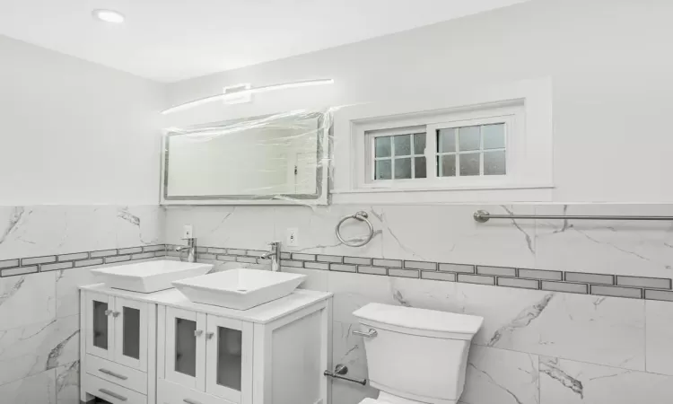 Bathroom featuring tile walls, vanity, and toilet