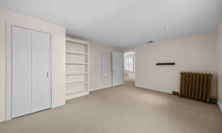 Unfurnished bedroom featuring a closet, radiator heating unit, and carpet floors