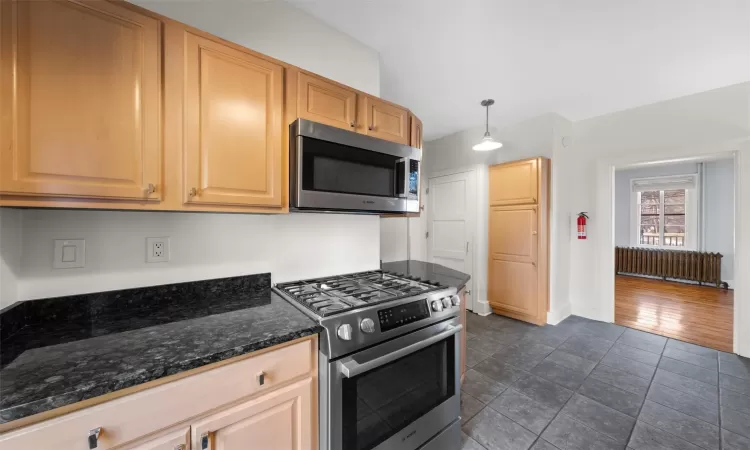 Kitchen featuring pendant lighting, dark stone counters, stainless steel appliances, and light brown cabinetry