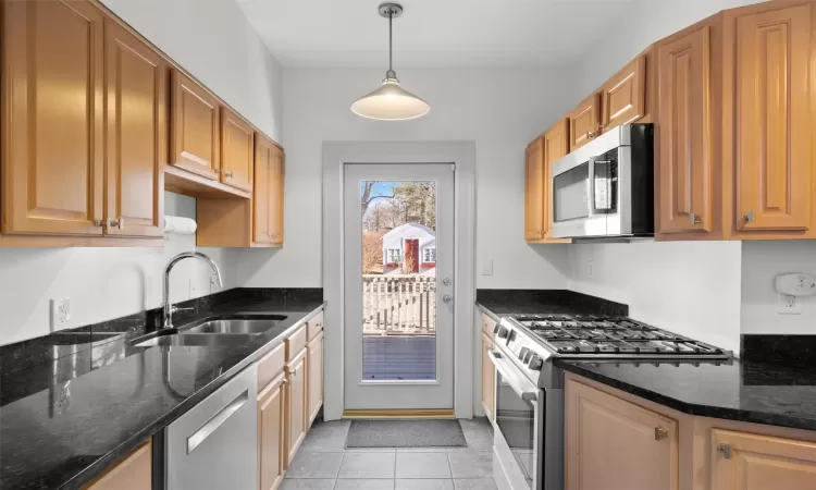 Kitchen featuring sink, stainless steel appliances, dark stone countertops, pendant lighting, and light tile patterned floors