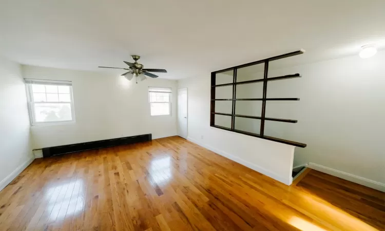 Unfurnished room featuring a baseboard heating unit, ceiling fan, and hardwood / wood-style floors