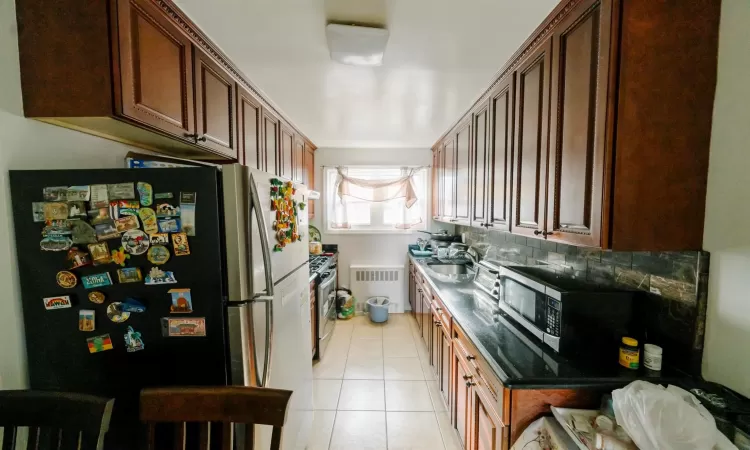 Kitchen with stainless steel appliances, decorative backsplash, radiator heating unit, and light tile patterned floors