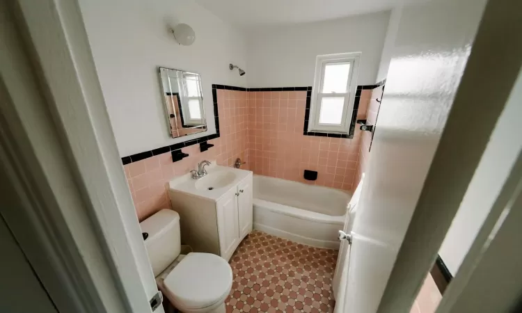 Full bathroom with toilet, vanity, tile walls, and tiled shower / bath combo