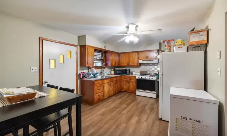 Kitchen featuring white fridge, ceiling fan, light hardwood / wood-style floors, stove, and decorative backsplash