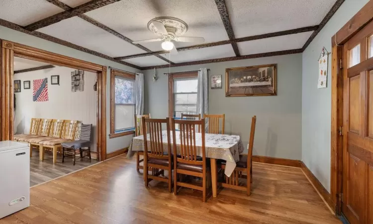 Dining space with a textured ceiling, light wood-type flooring, beam ceiling, ceiling fan, and coffered ceiling