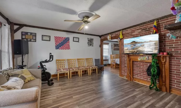 Living room with wood-type flooring, brick wall, ceiling fan, ornamental molding, and a textured ceiling