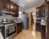 Kitchen with stainless steel appliances, dark brown cabinets, ventilation hood, light hardwood / wood-style flooring, and tasteful backsplash