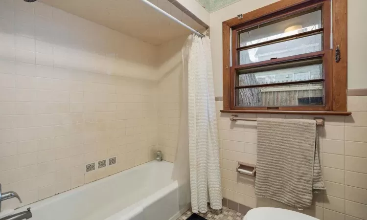 Bathroom featuring tile walls, shower / bath combination with curtain, and toilet