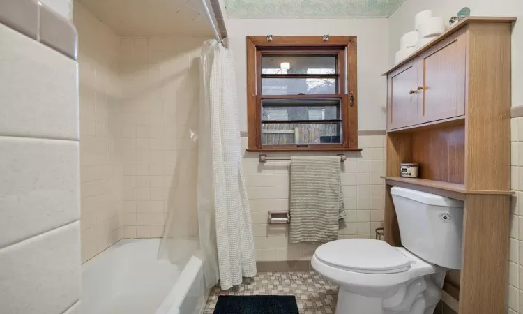 Bathroom with tile walls, toilet, and shower / tub combo