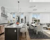 Kitchen with light stone countertops, wall chimney range hood, an island with sink, decorative light fixtures, and decorative backsplash