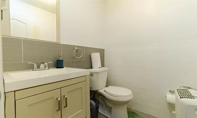 Bathroom with radiator, vanity, toilet, and tile walls