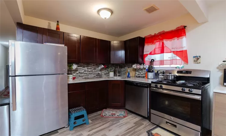 Kitchen featuring stainless steel appliances, sink, light hardwood / wood-style flooring, decorative backsplash, and dark brown cabinets