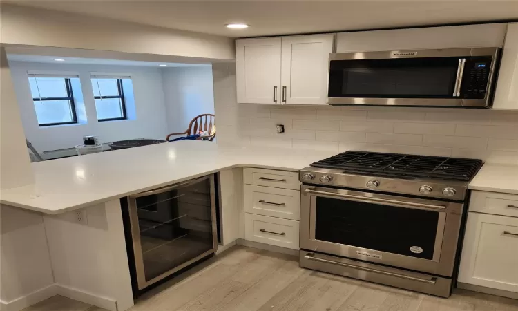 Kitchen with light hardwood / wood-style floors, tasteful backsplash, wine cooler, white cabinetry, and appliances with stainless steel finishes