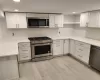 Kitchen with stainless steel appliances, light hardwood / wood-style flooring, white cabinetry, and tasteful backsplash