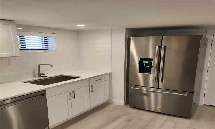 Kitchen with appliances with stainless steel finishes, light wood-type flooring, sink, white cabinets, and tasteful backsplash