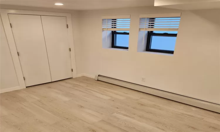 Unfurnished bedroom with baseboard heating, light hardwood / wood-style flooring, and a closet