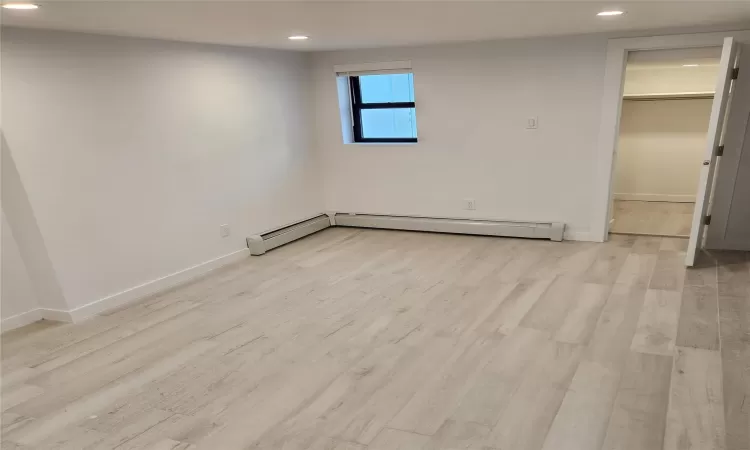 Unfurnished room featuring a baseboard radiator and light hardwood / wood-style flooring