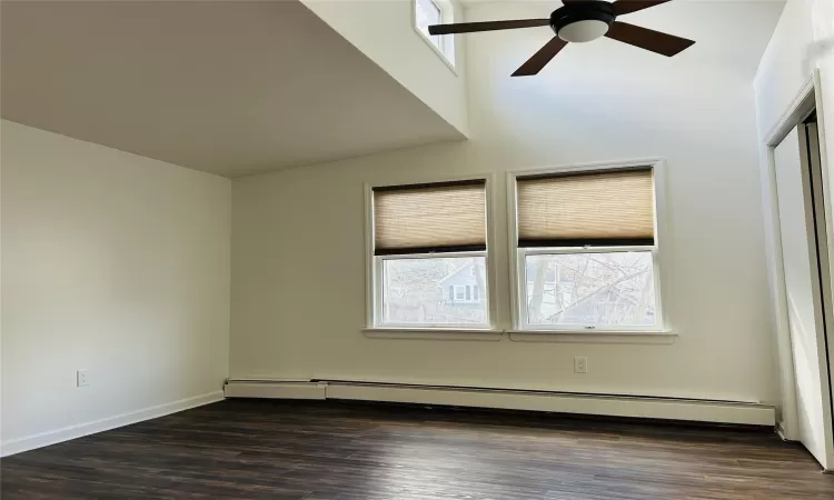 Empty room with ceiling fan, baseboard heating, a healthy amount of sunlight, and dark wood-type flooring