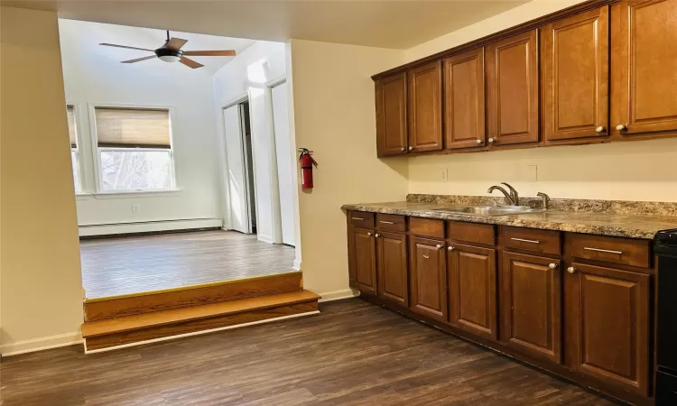 Kitchen with a baseboard heating unit, dark wood-type flooring, ceiling fan, and sink