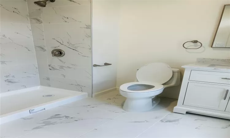 Bathroom featuring tiled shower, vanity, and toilet