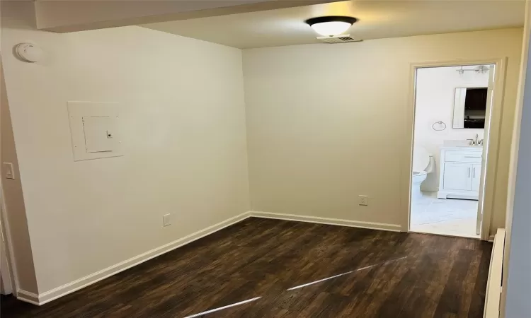 Unfurnished room with sink, baseboard heating, electric panel, and dark hardwood / wood-style floors