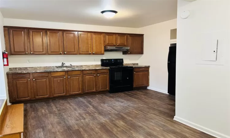 Kitchen featuring dark wood-type flooring, dark stone counters, black appliances, and sink