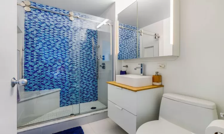 Bathroom with toilet, vanity, tile patterned floors, and a shower with shower door