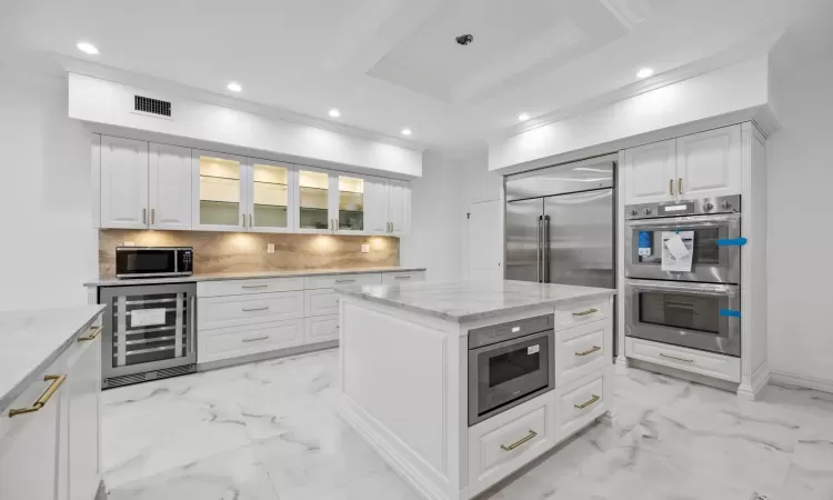 Kitchen with appliances with stainless steel finishes, white cabinets, beverage cooler, and a center island