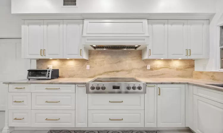 Kitchen featuring custom exhaust hood, gas cooktop, backsplash, and white cabinetry