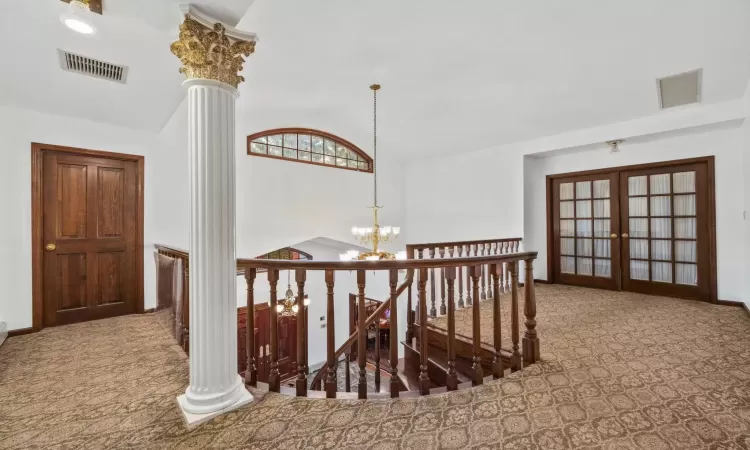 Hall featuring french doors, lofted ceiling, a chandelier, and ornate columns