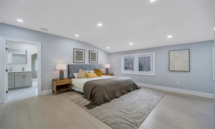 Bedroom with lofted ceiling, light wood-type flooring, and connected bathroom