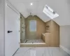 Bathroom featuring lofted ceiling with skylight, wooden walls, and tiled shower