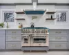 Kitchen with sink, range with two ovens, wall chimney exhaust hood, and gray cabinetry