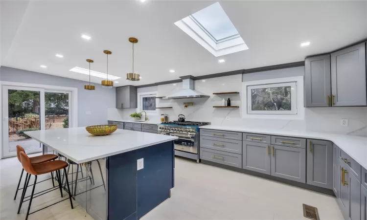 Kitchen with wall chimney exhaust hood, range with two ovens, decorative backsplash, and decorative light fixtures