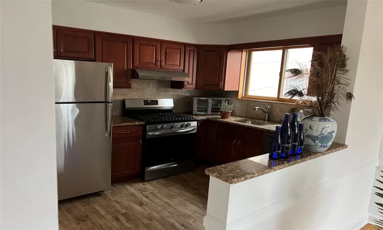 Kitchen with stainless steel appliances, dark stone counters, dark wood-type flooring, sink, and tasteful backsplash