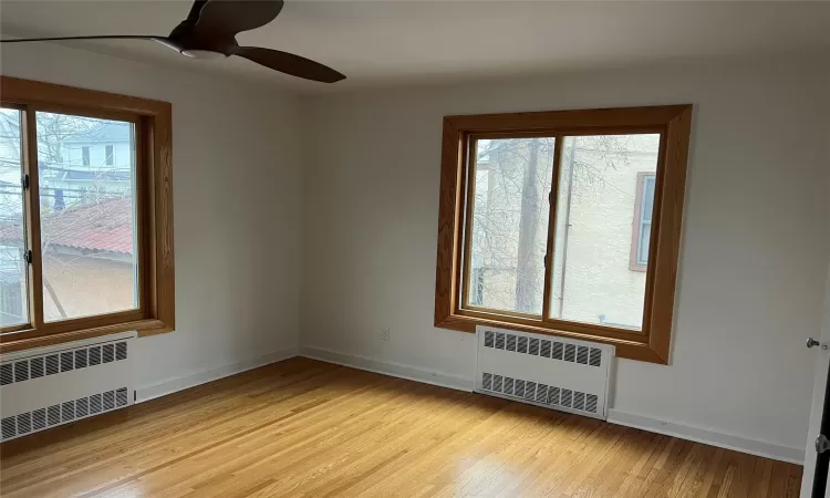 Unfurnished room featuring ceiling fan, radiator, and a wealth of natural light