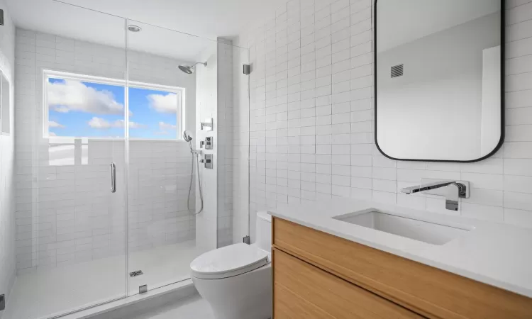 Bathroom with tile walls, tasteful backsplash, toilet, an enclosed shower, and vanity