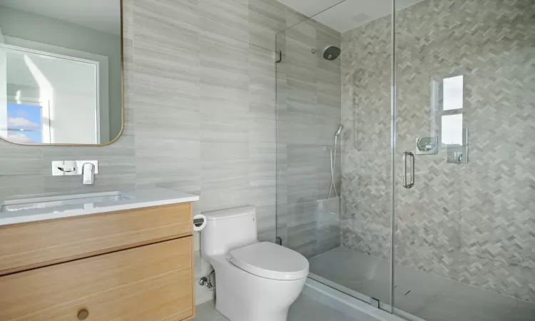 Bathroom featuring tile walls, an enclosed shower, vanity, and toilet