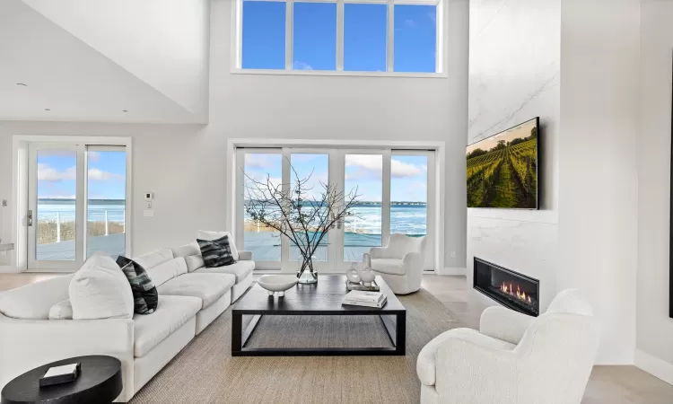 Living room featuring a towering ceiling, a high end fireplace, and a water view