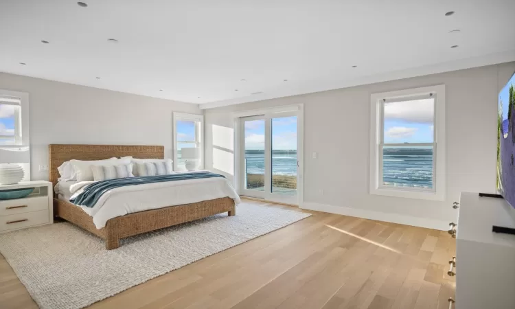 Bedroom with light hardwood / wood-style flooring, a water view, multiple windows, and access to exterior