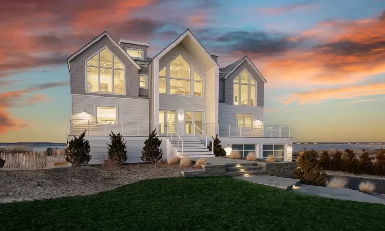 Back house at dusk featuring a balcony, a lawn, and a water view