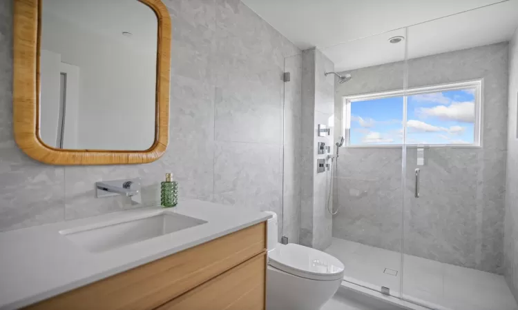 Bathroom with toilet, a shower with door, vanity, and tile walls