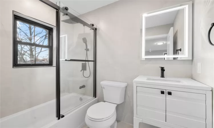 Full bathroom featuring tile walls, enclosed tub / shower combo, vanity, and toilet