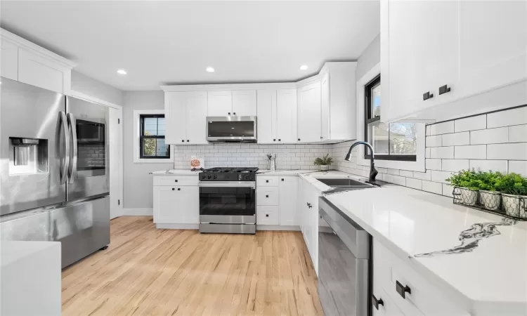 Kitchen with sink, white cabinetry, light hardwood / wood-style floors, decorative backsplash, and appliances with stainless steel finishes