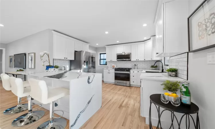 Kitchen featuring kitchen peninsula, a kitchen bar, white cabinetry, appliances with stainless steel finishes, and sink