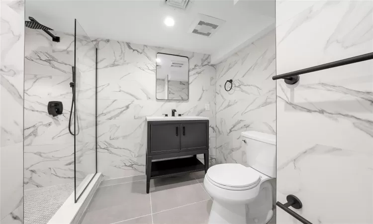 Bathroom featuring vanity, toilet, tiled shower, and tile patterned flooring