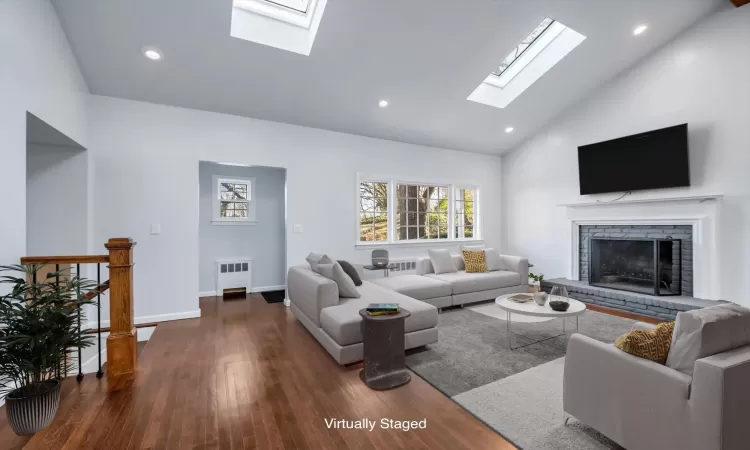 Living room with a brick fireplace, dark wood-type flooring, radiator, and high vaulted ceiling