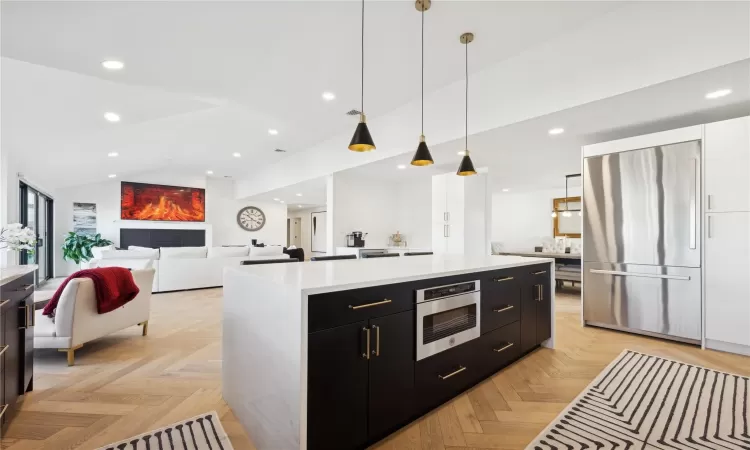 Kitchen featuring light parquet floors, lofted ceiling, built in refrigerator, hanging light fixtures, and a kitchen island